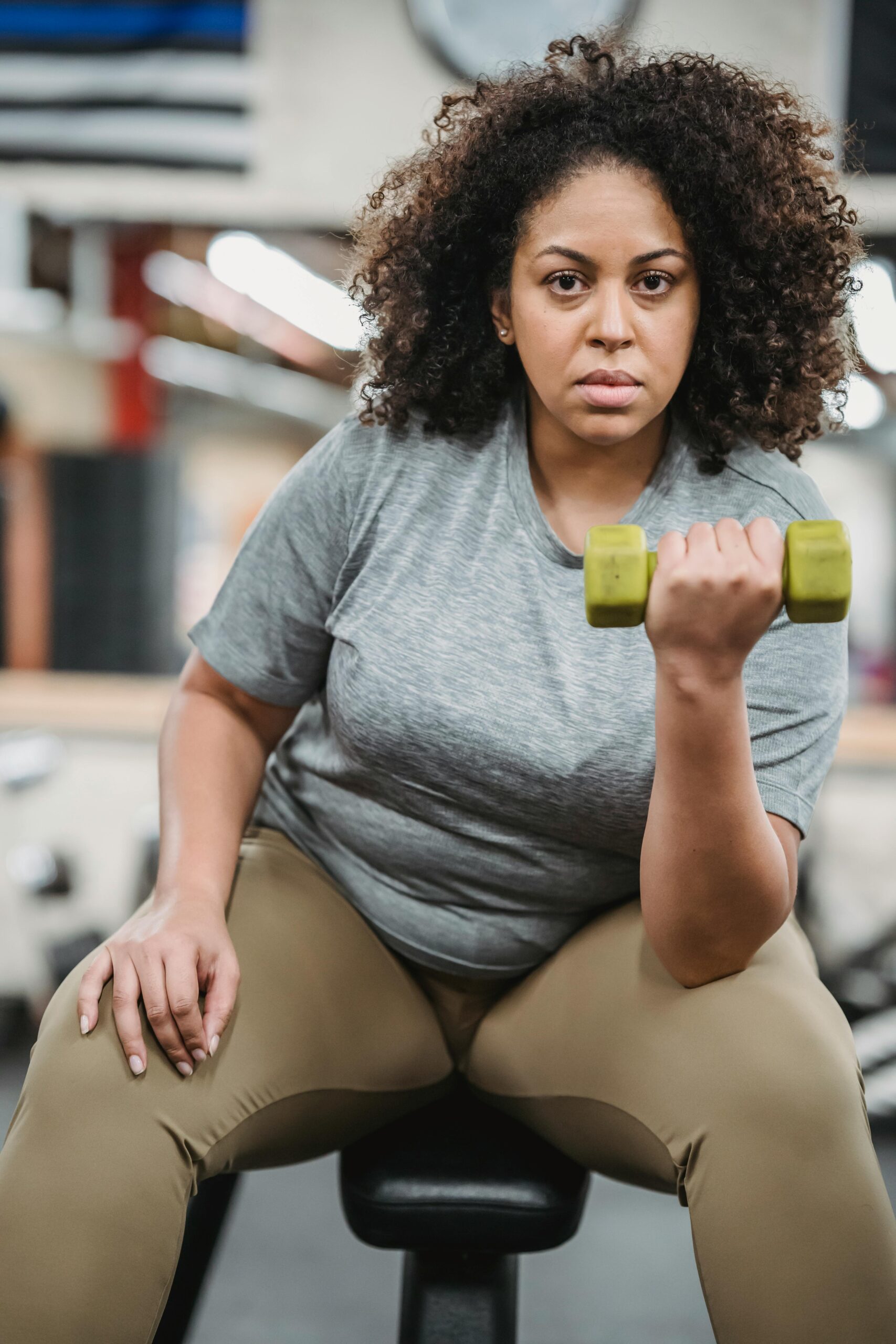 Focused woman exercising with a dumbbell, promoting fitness and strength in a gym setting.